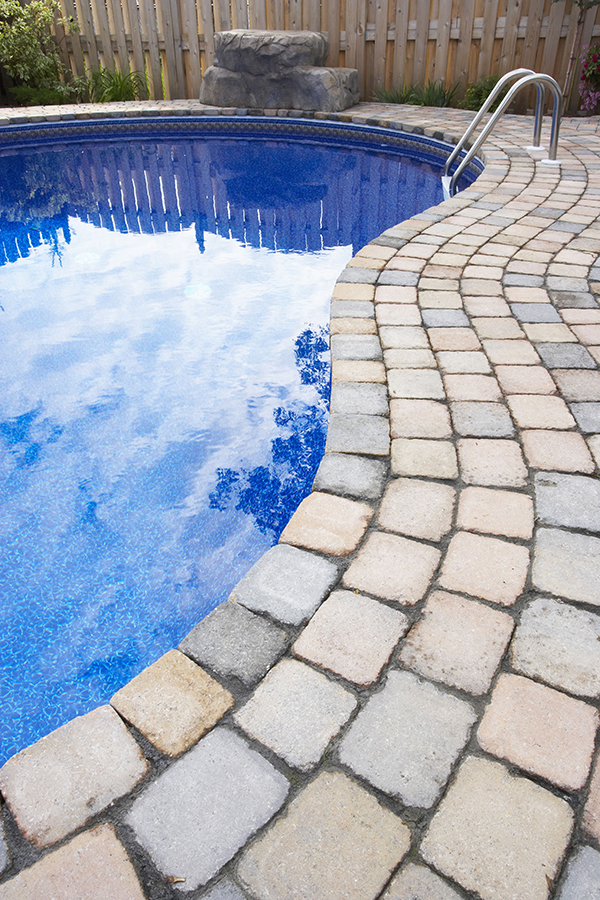 Curved inground pool edged with tumbled paver coping and a boulder feature